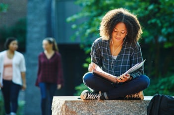 College student sitting cross legged reading and listening to music.
